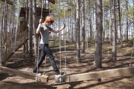 Rope training camp in the forest, a teenage girl walks on suspended swing bars.