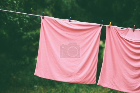 Pink pillowcases are dried in the garden on a rope with plastic clothespins.