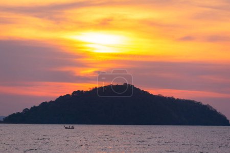 A captivating sunrise unfolds over the waters of Saphan Hin, bathing a solitary long-tail boat and Phuket silhouette in a warm, golden glow.