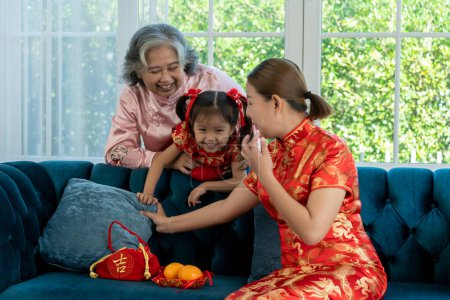 Photo for Happy Asian family with different generation in chinese traditional costume, grandmother playing with granddaughter and young mother sitting on sofa in living room, They are enjoy and smile together with fun, copy space - Royalty Free Image
