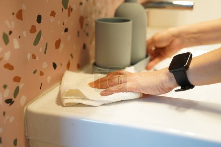 Cropped image, Close up Woman's hand using towel to clean wash basin and faucet in bathroom, arranged wash hand gel bottle, housekeeper working at home