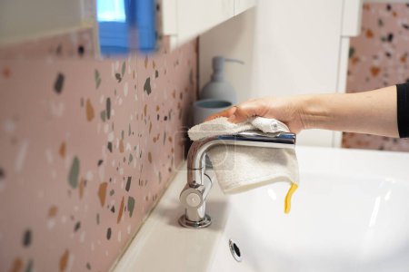 Cropped image, Close up Woman's hand using towel to clean wash basin and faucet in bathroom, arranged wash hand gel bottle, housekeeper working at home