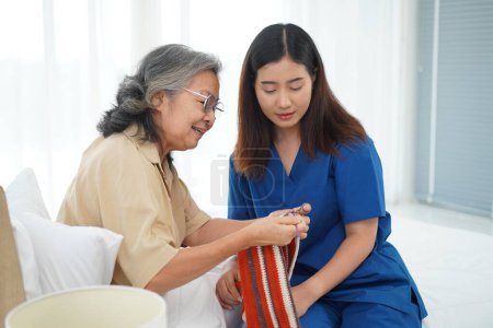 Photo for Asian senior woman sitting on bed in bedroom and crocheting in a handicraft as a hobby or occupational therapy, She teaching to Young female caregiver, They have fun together at home or nursing home - Royalty Free Image