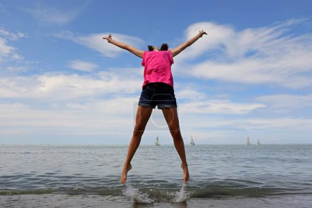 Photo for Happy girl jumping and rejoicing for joy by the sea in summer - Royalty Free Image