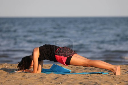 Foto de Joven chica de pie inmóvil en la posición llamada Plank durante el ejercicio gimnástico junto al mar - Imagen libre de derechos