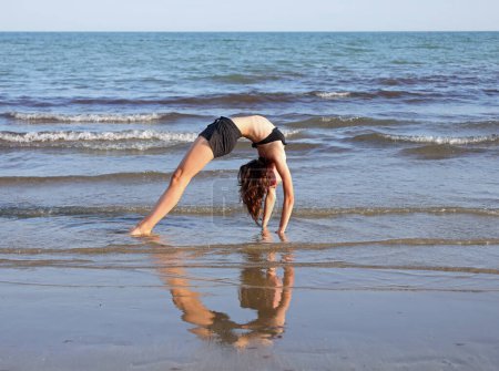 Photo for Young girl upside down and forms a heart with the body and reflection on the beach - Royalty Free Image