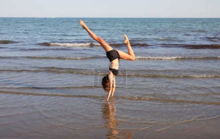 Téléchargez les photos : Fille mince dos à dos tout en faisant des exercices de méditation de yoga et de faire symbole OM avec les mains près de la mer en été - en image libre de droit