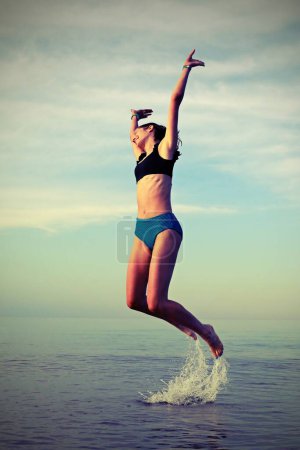 Photo for Young girl jumps for joy on the sea with old toned effect - Royalty Free Image