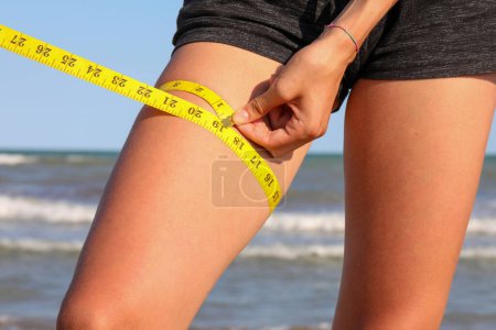 Photo for Measurement of the thigh circumference of the leg of young girl with  tape measure and measures in inches - Royalty Free Image