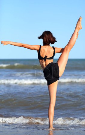 Photo for Girl does gymnastic exercises on the sandy beach by the sea in summer - Royalty Free Image