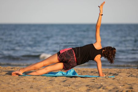 Foto de Niña entrenando junto al mar en verano en la colchoneta del gimnasio en la playa al atardecer - Imagen libre de derechos