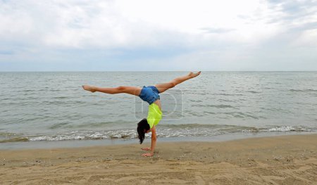 Photo for Young girl does the gymnastic cartwheeling in the summer by the sea - Royalty Free Image