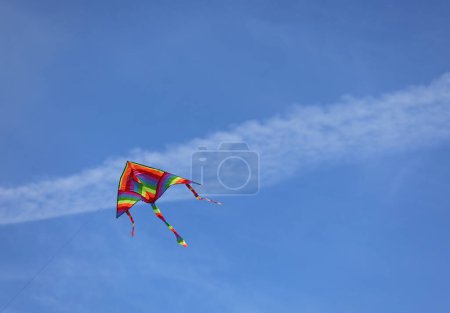 Foto de Big kite with rainbow colors flies tied on string in the blue sky - Imagen libre de derechos