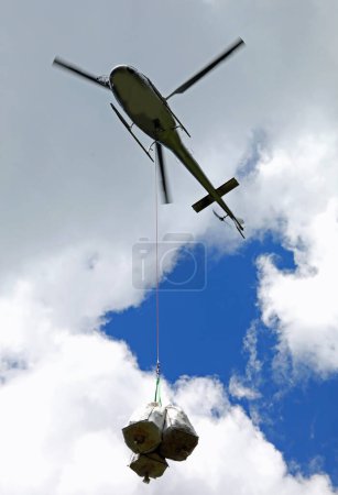 Photo for Helicopter in flight while transporting the goods attached to the winch and the steel cable - Royalty Free Image