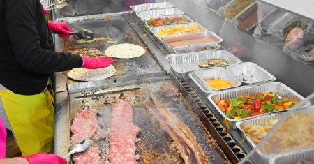 Photo for Cooks that cook street food with meat and vegetables in the hot metal plate in the stall at the fair - Royalty Free Image