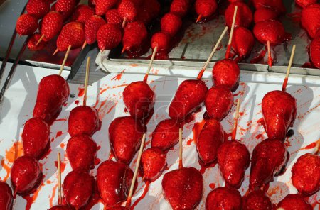 Téléchargez les photos : Skewers of large red ripe caramelized strawberries with sugar on top for sale in candy stall - en image libre de droit