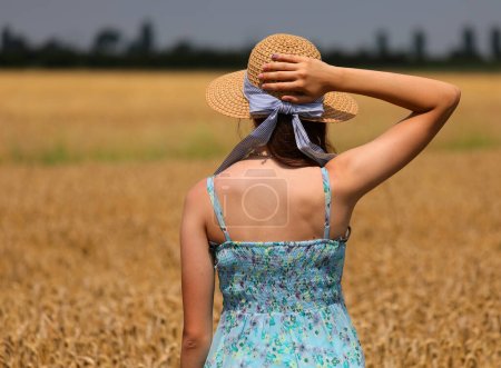 Photo for Young girl in straw hat and short dress points in the middle of the ripe wheat field in summer - Royalty Free Image