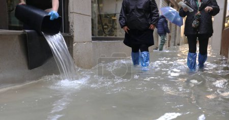 Hochwasser in Venedig in Norditalien, während Menschen mit einem Eimer das Wasser aus den Geschäften entleeren