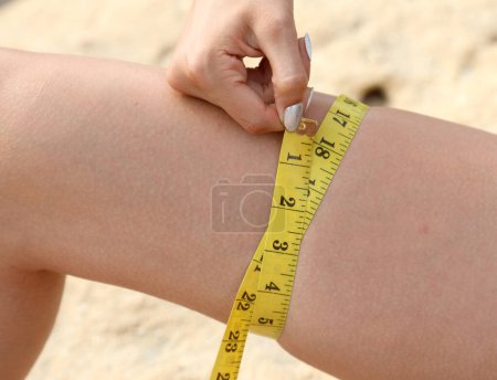 Photo for Thihg of a slender girl while measuring with yellow meter and measure in inches - Royalty Free Image