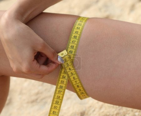 Photo for Slender thigh of young woman measured with yellow tape measure and numbers in CENTIMETERS - Royalty Free Image