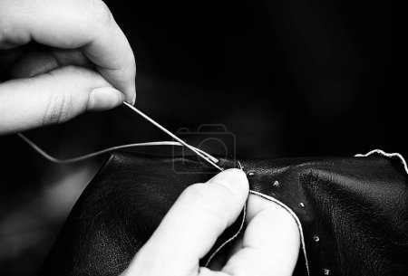 Photo for Young hands sew and mend the piece of leather with black and white effect - Royalty Free Image