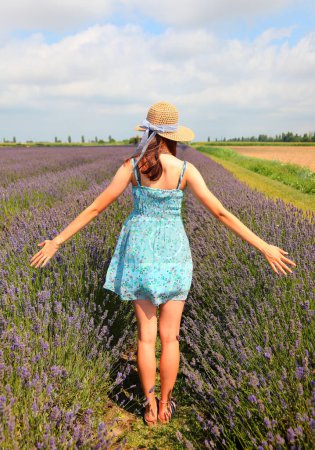 Photo for Young girl wearing summer dress and straw hat in lavender flower field in the countryside in summer - Royalty Free Image