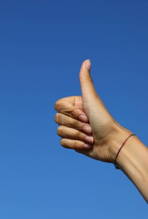 Téléchargez les photos : Main de fille avec pouce vers le haut signifiant parfait ou succès et ciel bleu - en image libre de droit