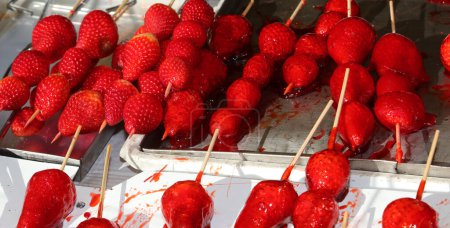 Téléchargez les photos : Skewers of large red ripe caramelized strawberries with sugar on top for sale in candy stall - en image libre de droit