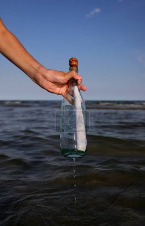 Photo for Boy takes a bottle with a secret message on the sea in summer - Royalty Free Image