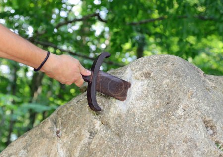 Foto de Mano extrae la espada atascada en la roca como en la historia mitológica del rey Arturo - Imagen libre de derechos