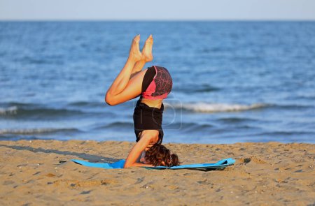 Foto de Chica joven boca abajo durante el entrenamiento en la playa junto al mar - Imagen libre de derechos