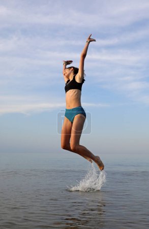 Photo for Young girl makes a big jump on the seashore symbol of gaiety and joy - Royalty Free Image