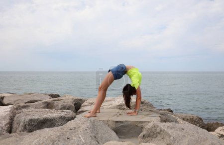 Photo for Young girl bending over backward in summer and sea on background - Royalty Free Image