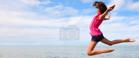 Photo for Young girl takes a big jump by the sea in summer in shorts - Royalty Free Image