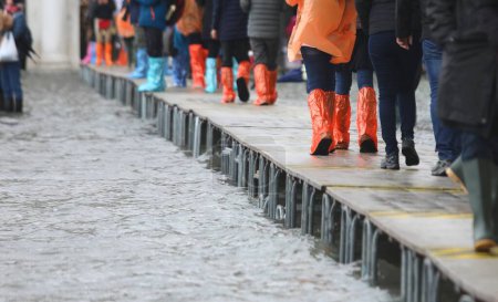 Photo for People in gaiters boots walking over elevated walkway during high tide Venice in Italy - Royalty Free Image
