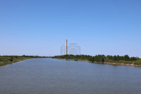 Photo for Porto Tolle, RO, Italy - July 5, 2023:Chimney of thermoelectric plant to production electric energy and Po River in Italian plain - Royalty Free Image