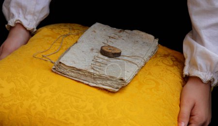 Photo for Ancient parchment closed with string and seal on a soft yellow cushion carried by the  hands of child - Royalty Free Image
