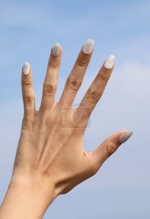 Téléchargez les photos : Cinq doigts de la main avec le fond du ciel bleu et vernis à ongles blanc sur les ongles - en image libre de droit