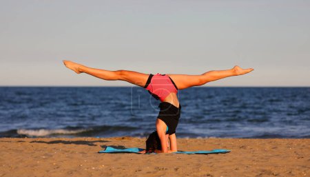 Foto de Niña realiza fracturas de piernas durante el entrenamiento en la playa y la puesta de sol por el mar - Imagen libre de derechos