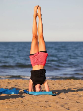 athletisches Mädchen führt am Strand am Meer im Sommer herausfordernde Gymnastikübungen in kurzen Hosen durch