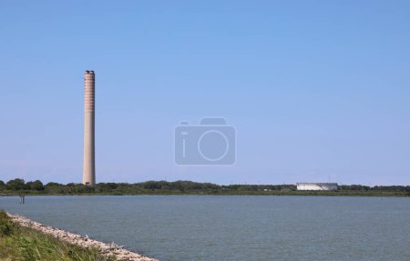 Foto de Porto Tolle, RO, Italia - 5 de julio de 2023: Chimenea alta de la planta termoeléctrica a la energía de producción y al titular del gas y al río Po - Imagen libre de derechos