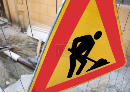 Téléchargez les photos : Panneau routier avec le pictogramme de l'homme travaillant près du chantier de construction de la route dans la ville - en image libre de droit