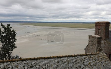 Photo for Elevated panoramic view from Mont Saint Michel Abbey in Normandy in Northern France and little people walkingn at low tide - Royalty Free Image