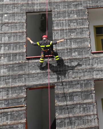 Photo for Fireman in harness climbs with rope and red helmet up a destroyed building - Royalty Free Image