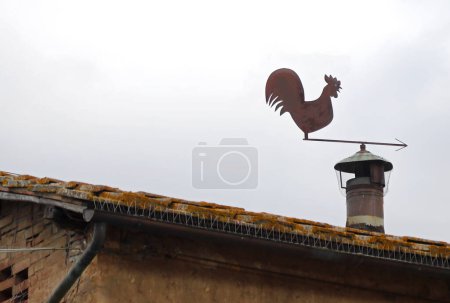 Téléchargez les photos : Girouette en fer comme une girouette en fer en forme de coq au-dessus de la cheminée d'un toit de maison - en image libre de droit