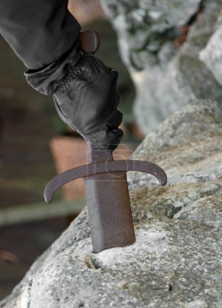 Téléchargez les photos : Main gantée du chevalier essayant d'extraire l'épée de la pierre avec ténacité et force - en image libre de droit