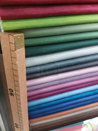 Téléchargez les photos : Échantillons de tissus de nombreuses couleurs dans la boutique de tissus et la mesure de compteur en bois utilisée par le tailleur pour prendre des mesures - en image libre de droit