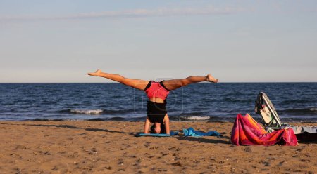 Foto de Chica joven realiza fracturas de piernas durante el entrenamiento en la playa y la puesta de sol - Imagen libre de derechos