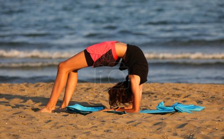 Photo for Young girl performing bodyweight gymnastics exercises on the beach at sunset - Royalty Free Image