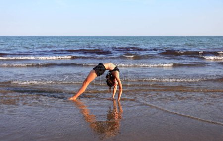 Photo for Girl while arching her back backwards to form a heart with body reflection on the wet beach - Royalty Free Image